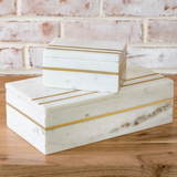 Marble boxes with gold stripes on a wooden surface with a brick wall background