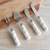 Set of four cheese tools with white marble handles on a wooden surface