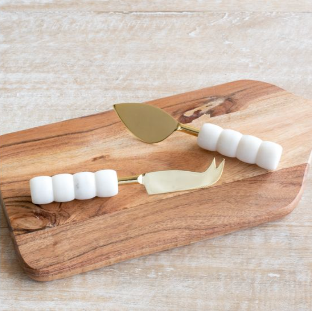 Wooden cutting board with gold cheese knives and white cheese on a light wooden surface