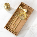 Gold cocktail shaker and tools in a cardboard box on a marble surface