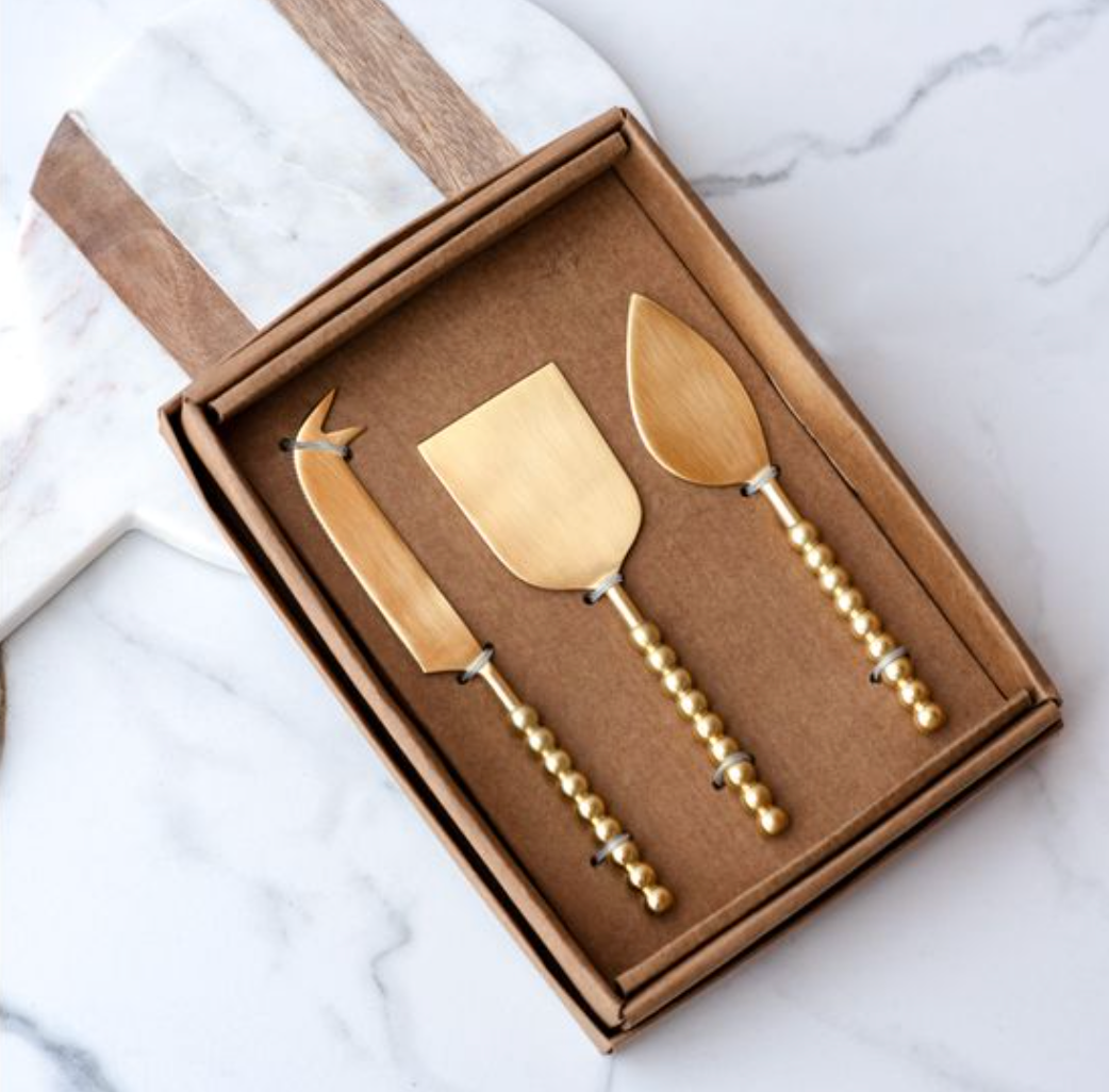 Set of three gold cheese knives in a box on a marble surface