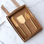 Set of three gold cheese knives in a box on a marble surface