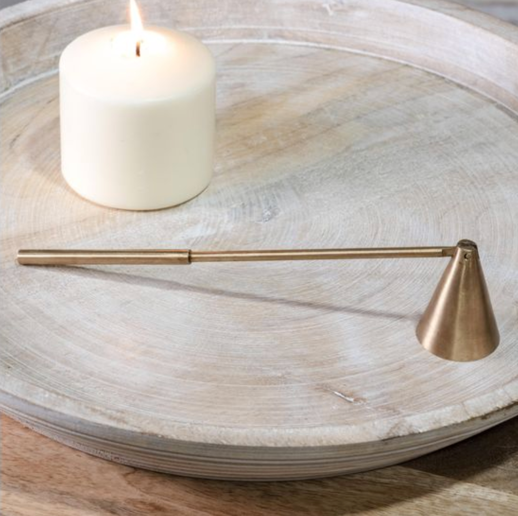 Brass candle snuffer on a wooden surface with a candle in the background