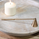 Brass candle snuffer on a wooden surface with a candle in the background
