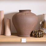 Collection of ceramic vases and bowls on wooden shelves against a white wall.