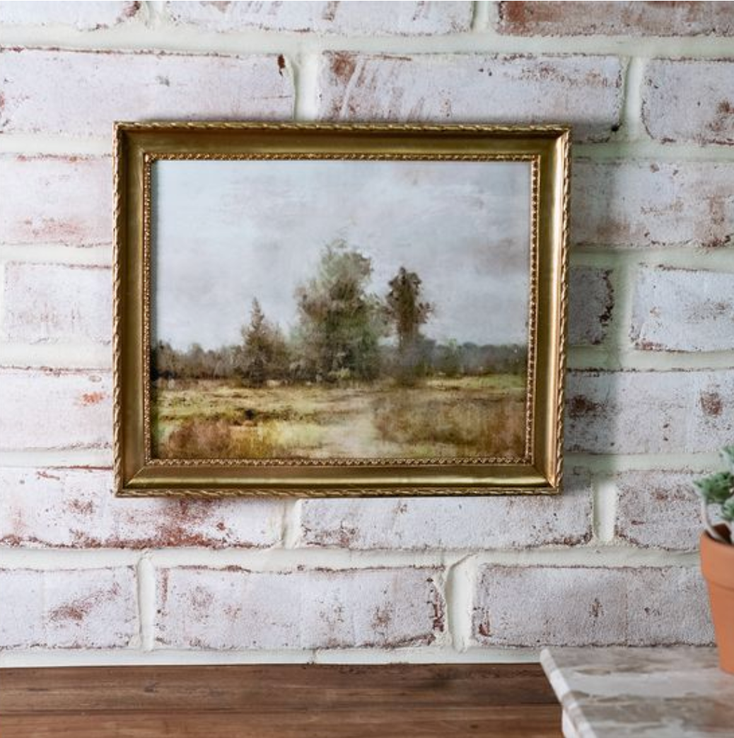 Framed 8x10 prairie landscape print featuring soft, muted countryside scenery with trees and open fields, displayed in a gold ornate frame against a whitewashed brick wall.