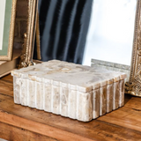 Closed rectangular marble box with scalloped lid and ribbed sides, crafted from warm-toned leopard marble, displayed on a wooden surface in front of decorative mirrors.