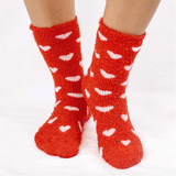 Red socks with white heart patterns worn by a person on a white background