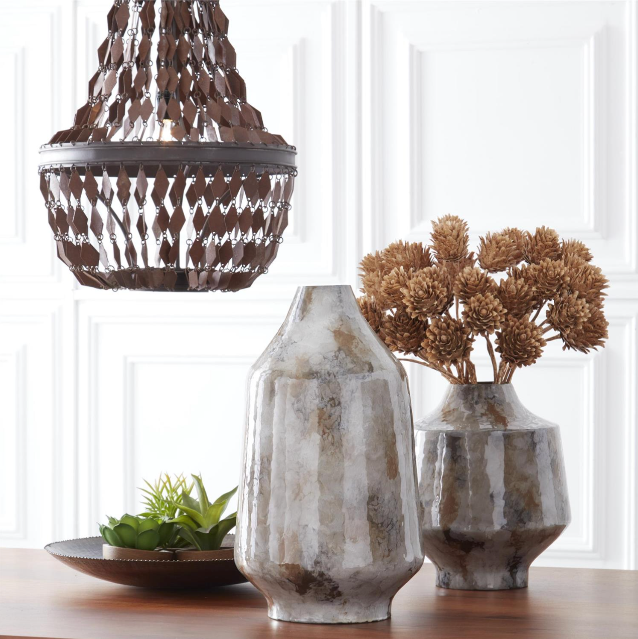 Decorative vases and a chandelier on a wooden surface with a white paneled wall background.