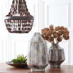 Decorative vases and a chandelier on a wooden surface with a white paneled wall background.