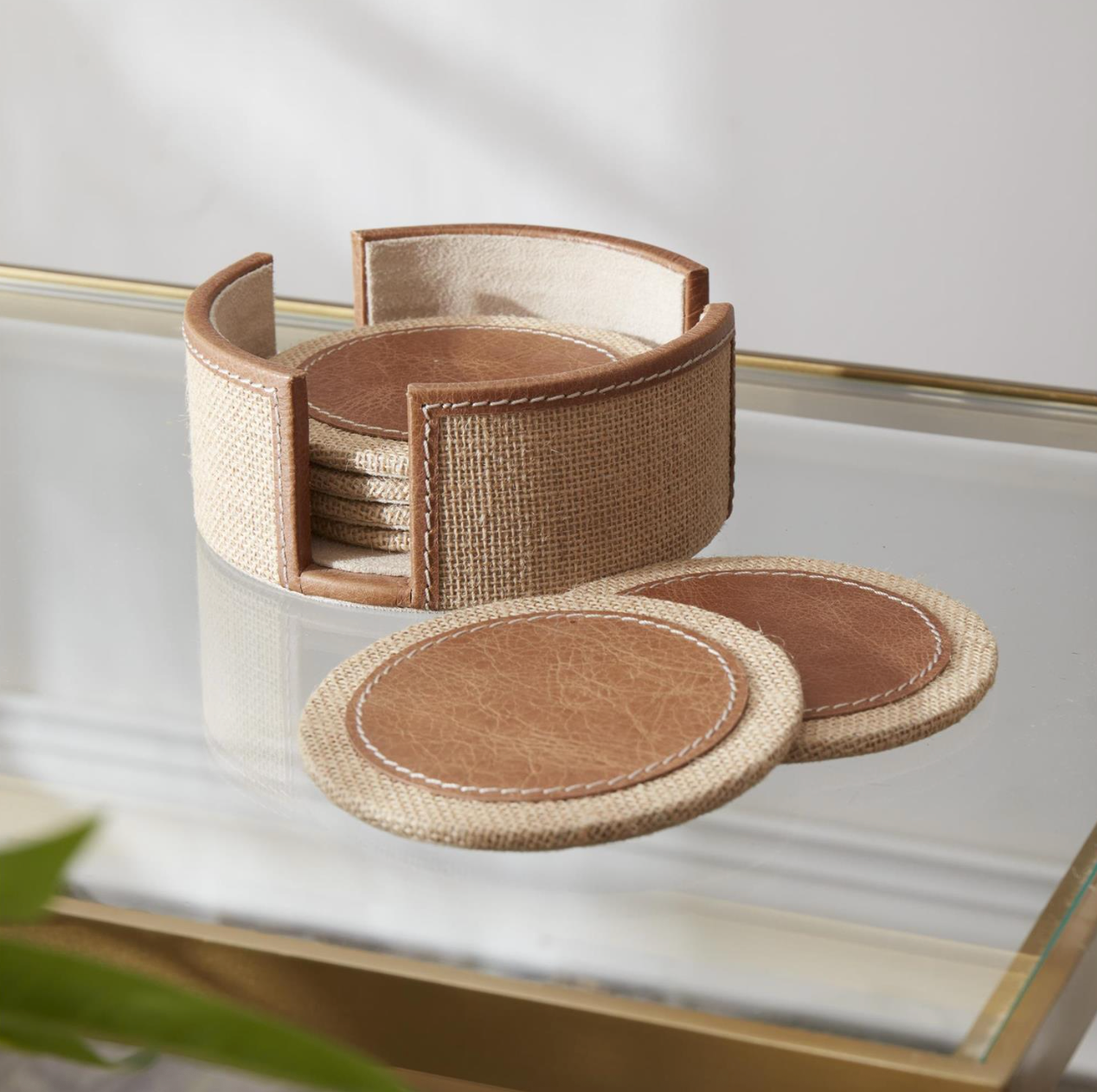 Set of brown coasters with a woven holder on a glass surface.