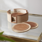 Set of brown coasters with a woven holder on a glass surface.