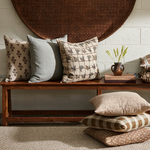 Decorative pillows on a wooden bench against a white brick wall.