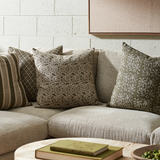 Gray sofa with patterned cushions against a light brick wall.