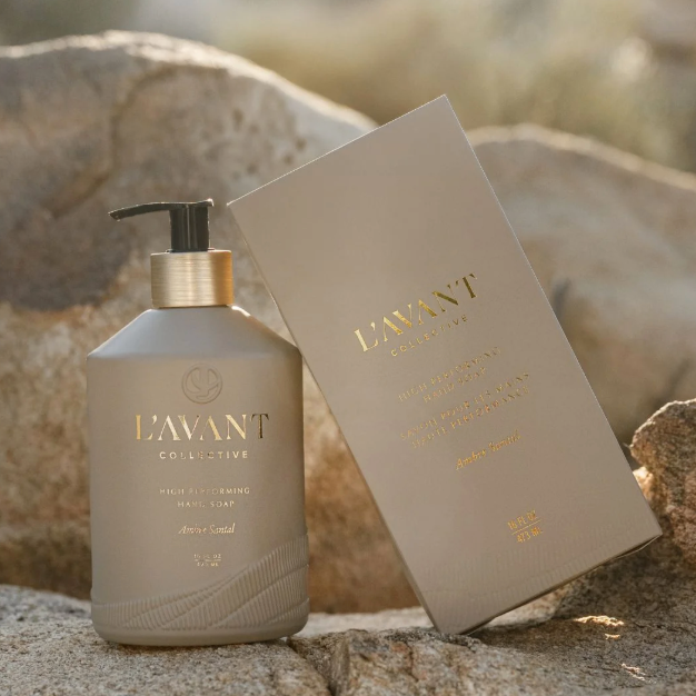 L'avant Collective hair care bottle and its matching box displayed outdoors on a rocky surface with a blurred natural background.