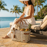 Woman sitting by the ocean with a woven bag containing fruits and a bottle, palm trees in the background