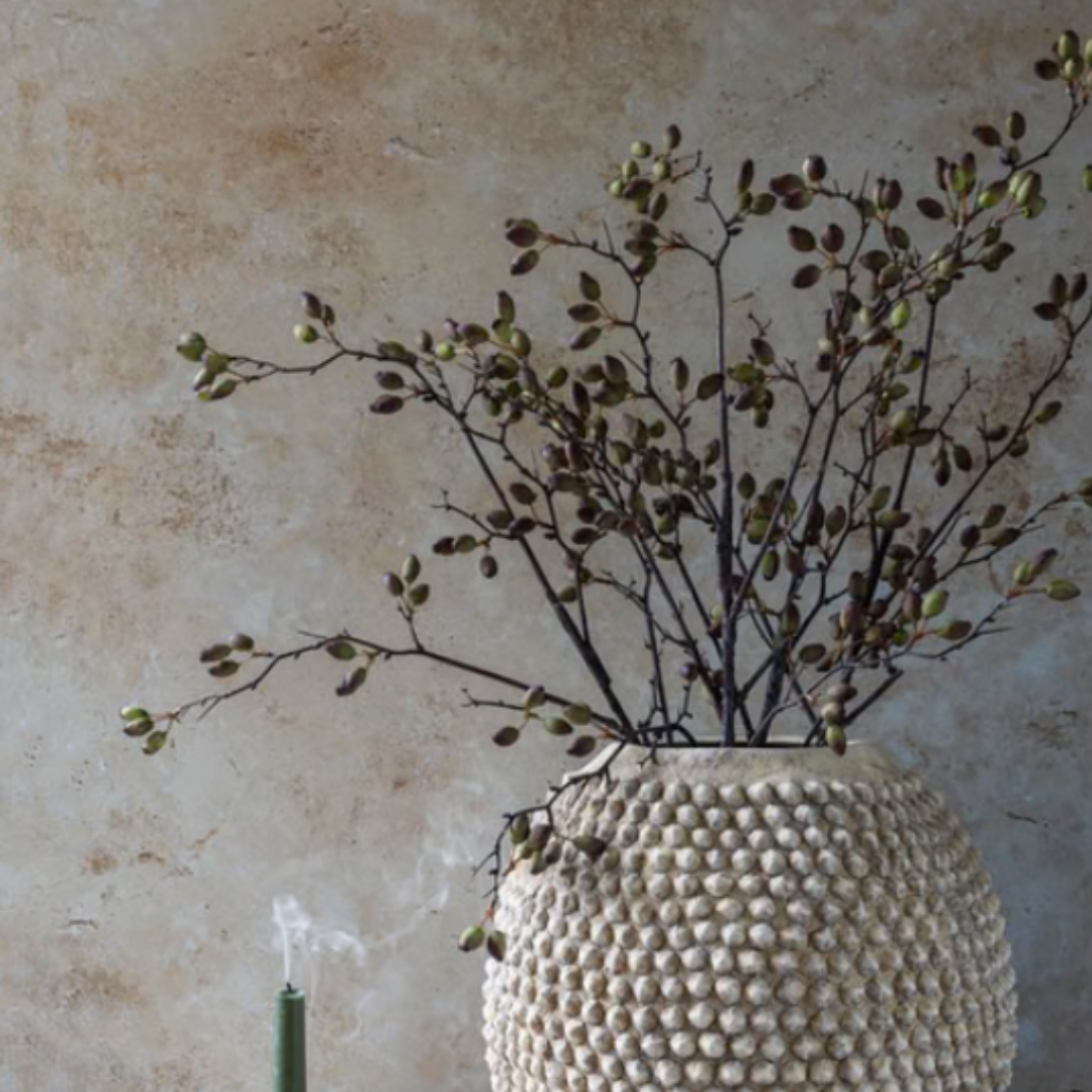 Textured vase with dried branches against a beige wall