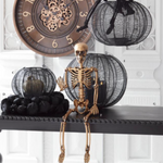Halloween-themed decor with skeleton figure, black wire pumpkins, and clock on a white background
