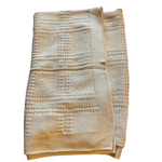 Neutral beige cotton knit baby blanket with a plaid-inspired textured pattern and ribbed border, folded neatly on a white background.