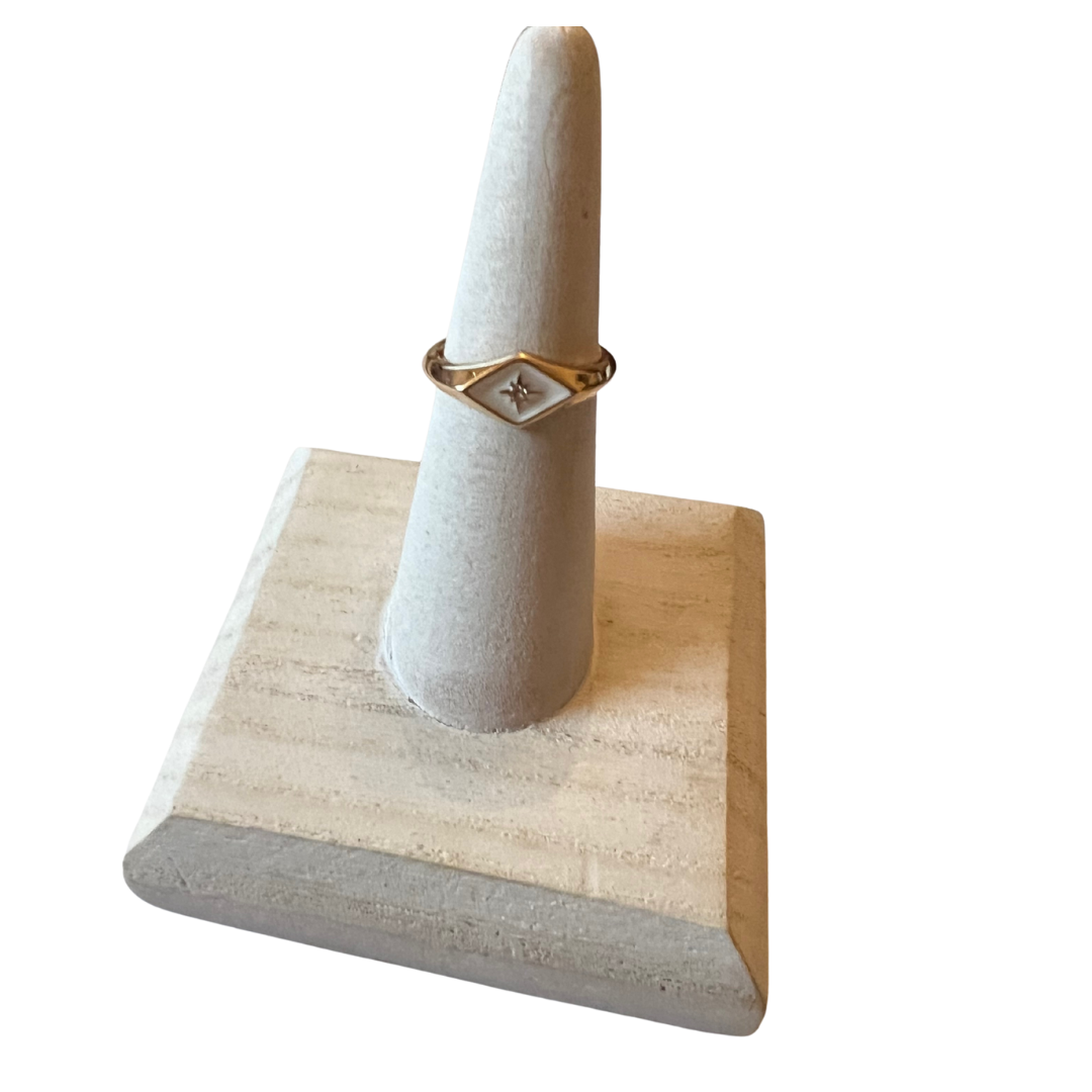 Gold ring on a white cylindrical stand with a wooden base against a white background
