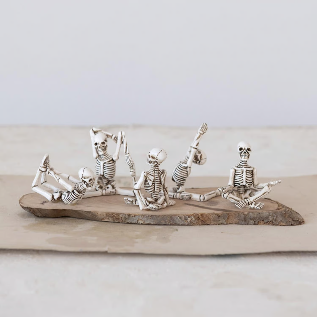 Silver skeleton figurines in various poses on a wooden board against a light background