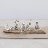 Silver skeleton figurines in various poses on a wooden board against a light background