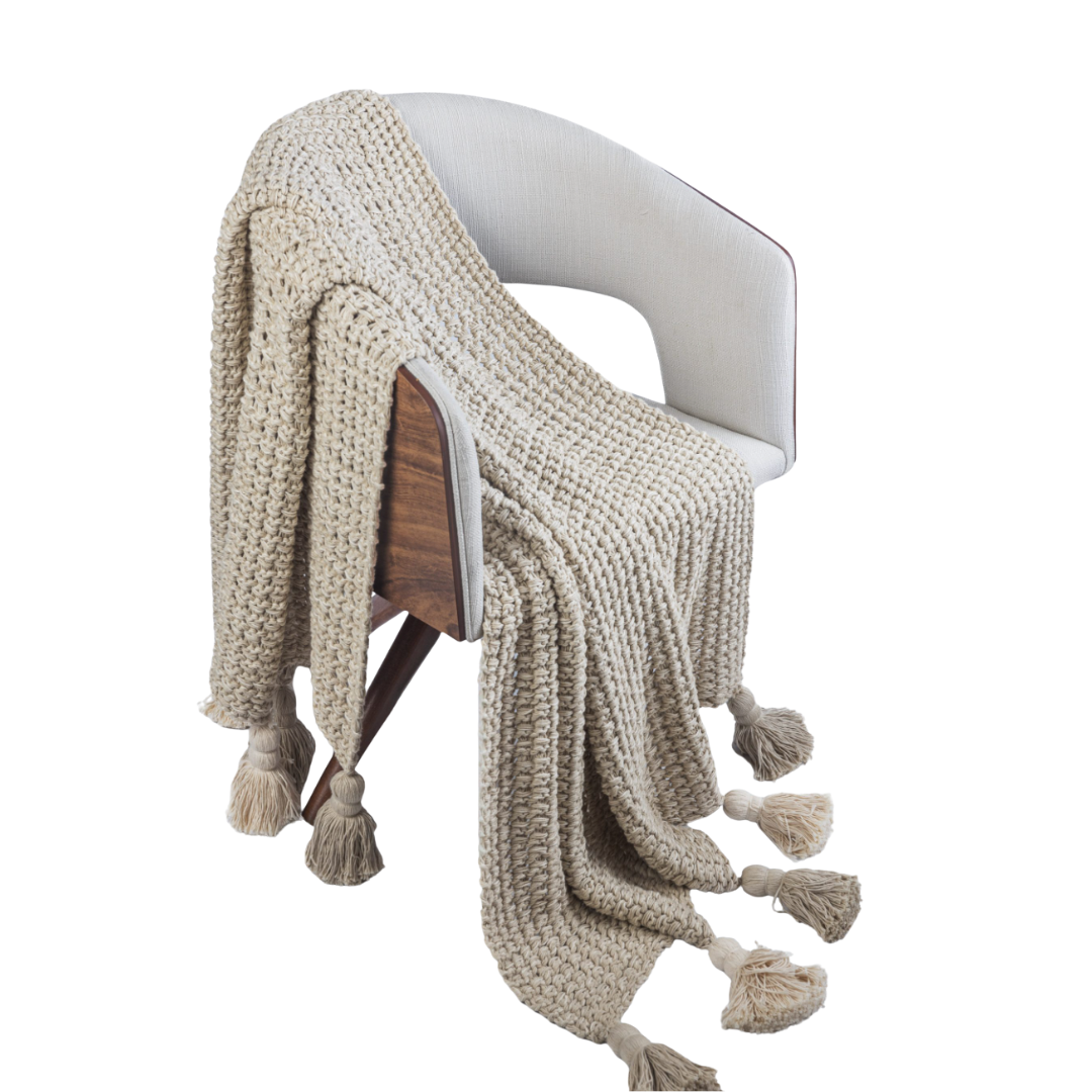 Beige knitted blanket with tassels draped over a chair on a white background