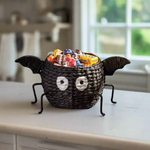 Halloween-themed candy basket shaped like a bat with candy inside on a white background