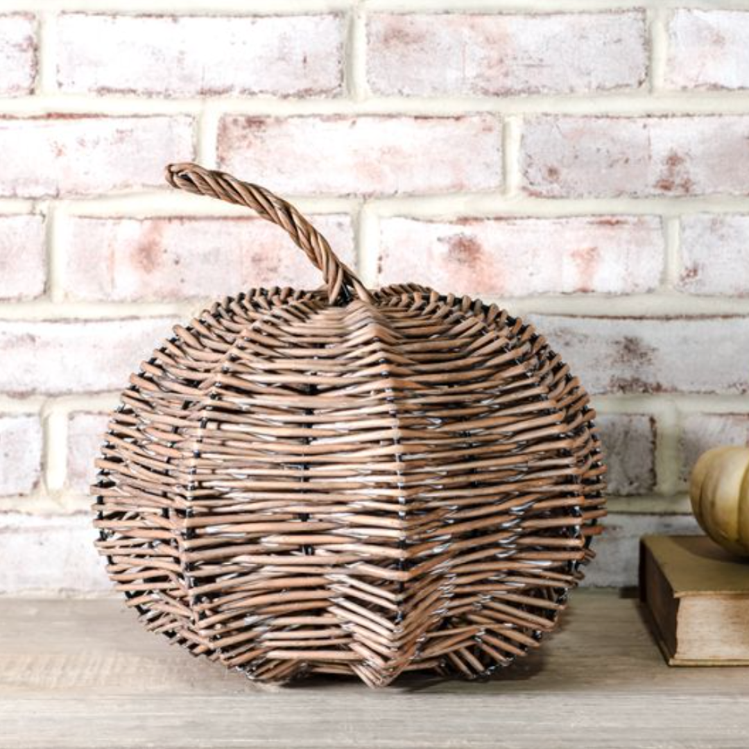 Wicker pumpkin on a wooden surface against a brick wall.