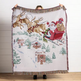 Woven blanket with Santa Claus and reindeer design being held with a white wall behind