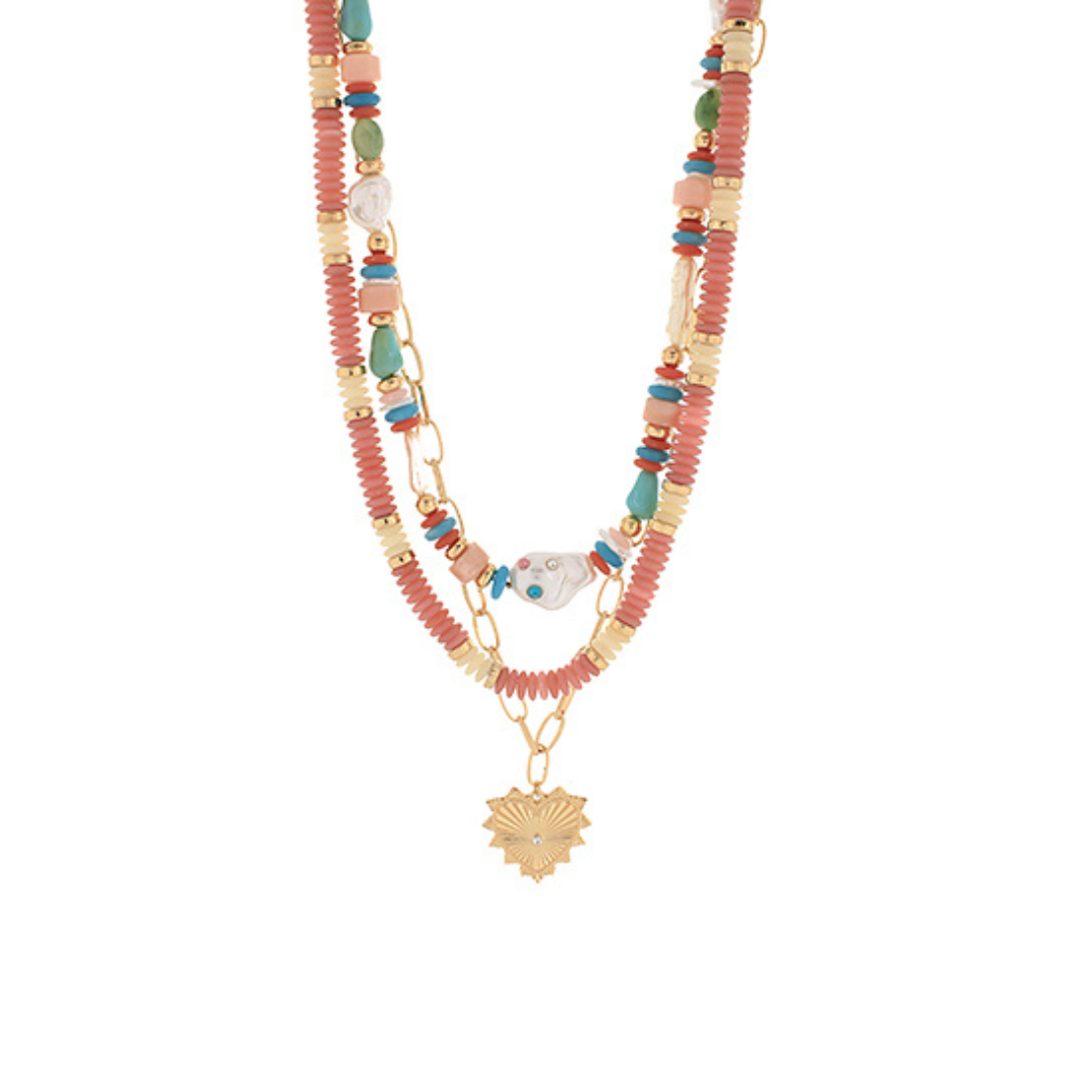 Layered beaded necklace with coral, turquoise, and gold beads, featuring a gold heart pendant and mixed textures on a white background