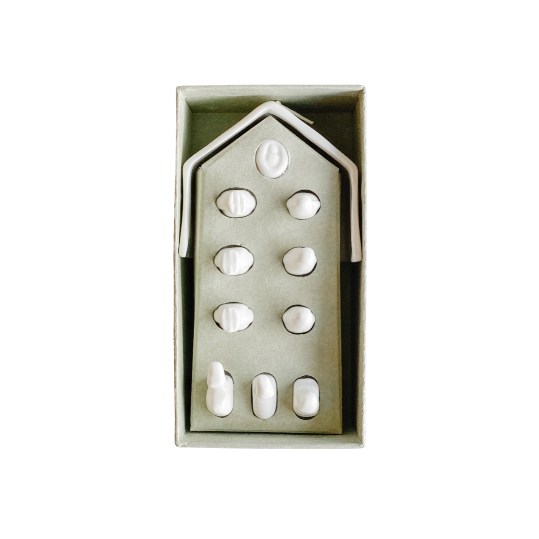 Minimalist white porcelain nativity scene with 11 handcrafted figures, including Mary, Joseph, Baby Jesus, Wise Men, animals, and a star-topped stable, displayed beside an eco-friendly kraft gift box