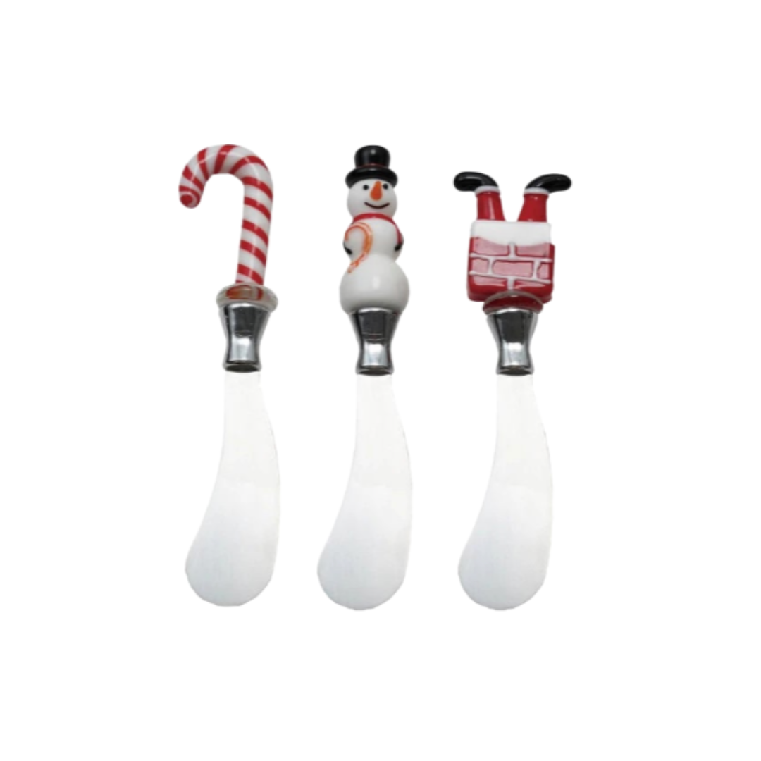 Three Christmas-themed ceramic spreaders with candy cane, snowman, and Santa Claus handles on a white background.