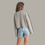 Person wearing a gray sweater and denim shorts on a plain background