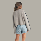 Person wearing a gray sweater and denim shorts on a plain background