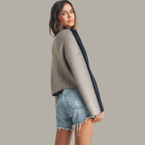 Woman wearing a gray sweater with navy sleeves and denim shorts on a plain background