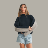 Woman wearing a black sweater with a unique design, holding a beige and brown bag against a gray background