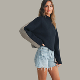 Woman wearing a black sweater and denim shorts against a gray background