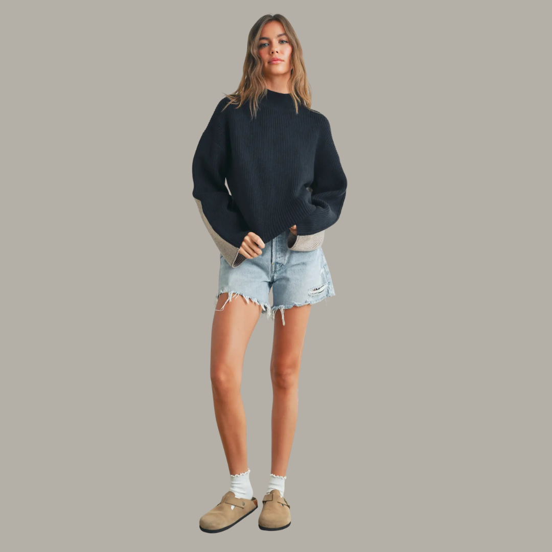 Woman wearing a navy sweater, denim shorts, and beige shoes on a gray background