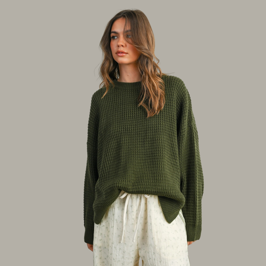 Woman wearing a green sweater and white pants against a gray background