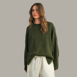 Woman wearing a green sweater and white pants against a gray background