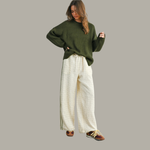 Woman wearing a green sweater and white pants on a gray background