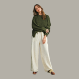 Woman wearing a green sweater and white pants on a gray background