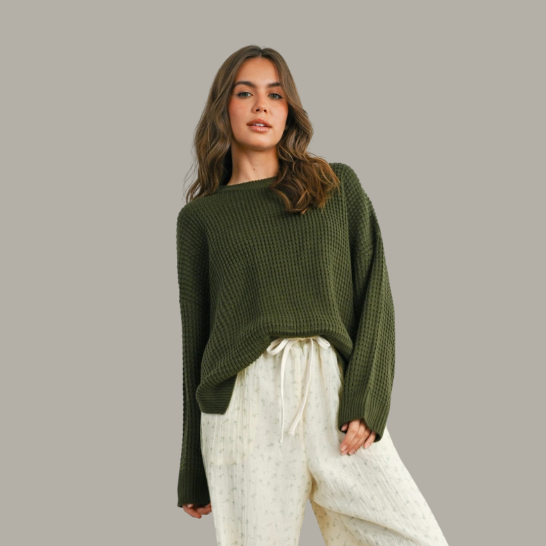 Woman wearing a green sweater and white pants against a gray background