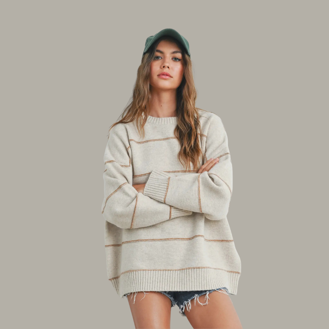 Woman wearing a light-colored sweater with brown stripes and a cap on a plain background