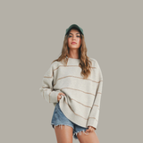 Woman wearing a cream sweater with brown stripes and denim shorts on a gray background