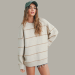 Woman wearing a beige sweater with brown stripes and a green cap against a gray background