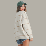 Woman wearing a striped sweater and denim shorts with a green cap on a gray background