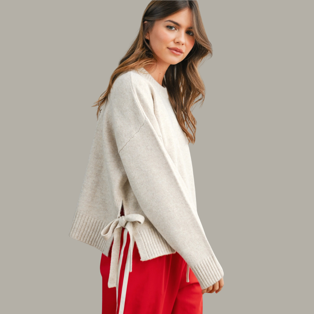 Woman wearing a beige sweater with a tie detail on a gray background