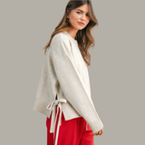 Woman wearing a beige sweater with a tie detail on a gray background